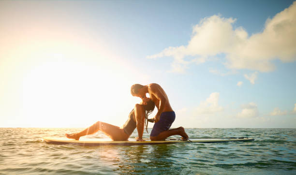 Couple sitting on paddleboard in ocean kissing at sunset 